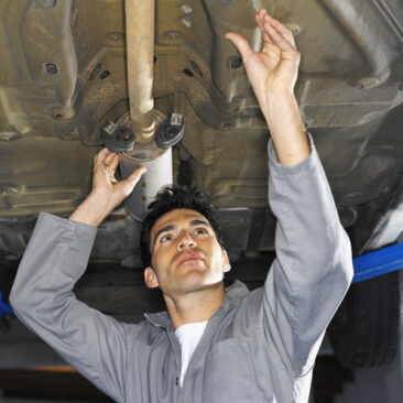 Low angle view of a male mechanic fixing an exhaust pipe on a car